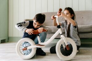 Two children engaged in assembling a white bicycle indoors, reflecting teamwork and focus.