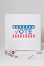 Ballot box with 'Vote' sign and voting stickers on a white background.