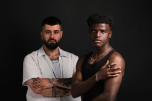 Portrait of two diverse men with tattoos posing in a studio setting, showcasing personal style.