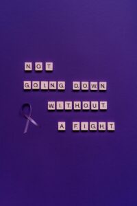 Scrabble tiles form motivational quote on purple background with awareness ribbon.
