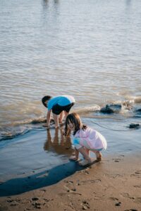 Kids play barefoot on a sunny beach, enjoying the water and sand.
