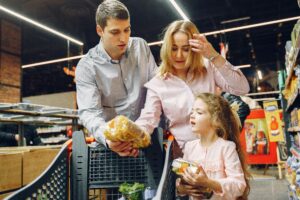A family enjoying shopping in a supermarket aisle, selecting groceries with a cart.