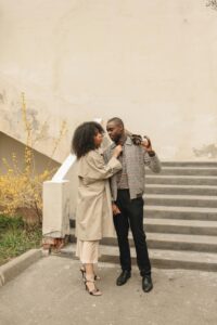 A fashionable couple standing and interacting lovingly on outdoor stairs.